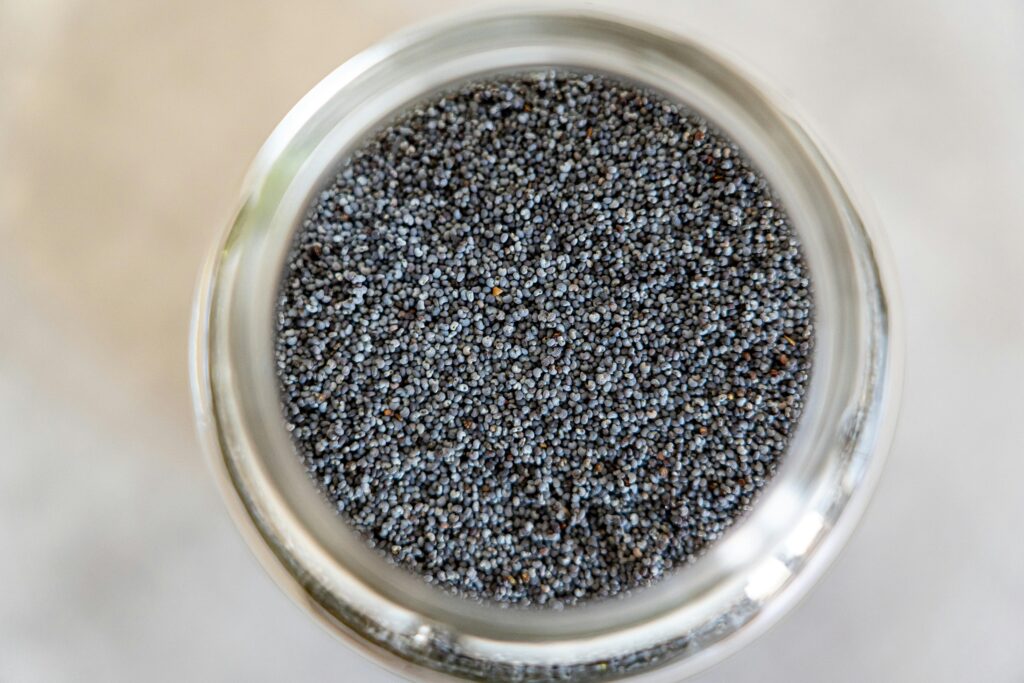 A detailed close-up of poppy seeds in a glass jar, highlighting texture and color.