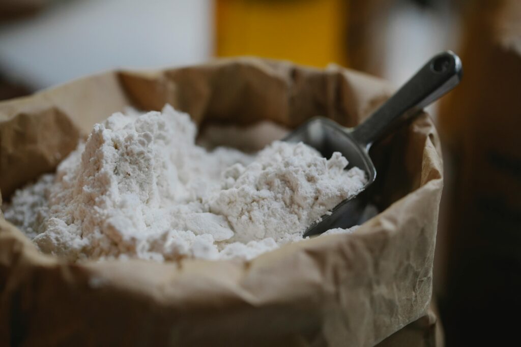 Close-up of a paper bag filled with flour with a metal scoop, perfect for home baking.