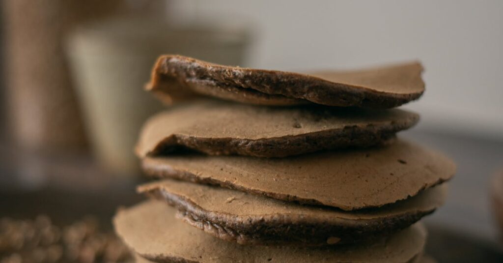 Delicious homemade chocolate buckwheat pancakes stacked on a wooden board with buckwheat grains.